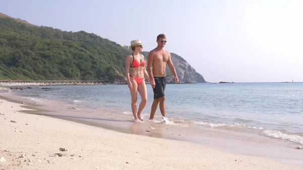 Una pareja está caminando por la playa, tomados de la mano, un hombre y una mujer. Turistas en el mar están descansando . —  Fotos de Stock