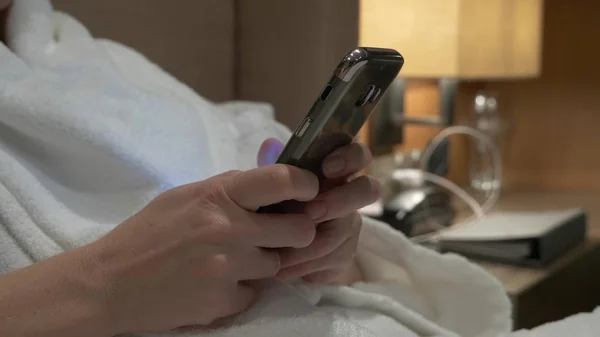 Close-up de mãos de mulher jovem digitando sms rolando imagens de telefone. as mãos femininas usam um smartphone à noite na cama — Fotografia de Stock