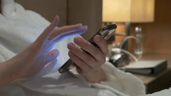 Крупный план молодой женщины руки печатая смс прокрутки фотографии телефона. женские руки используют смартфон вечером на кровати — стоковое фото