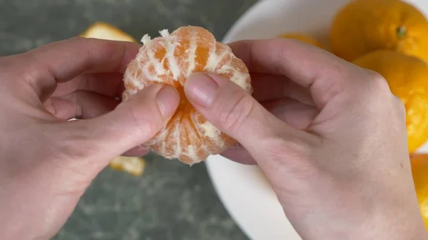 womens hands peel the peel of mandarins, mandarin slices are piled in a bowl