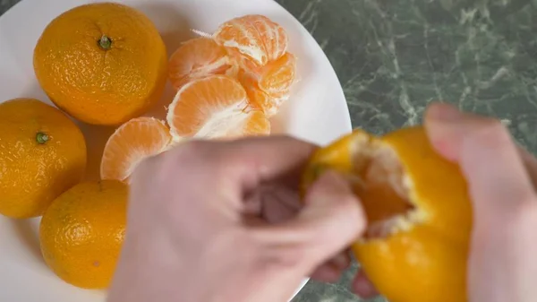 Le mani delle donne sbucciano la buccia dei mandarini, le fette di mandarino sono ammucchiate in una ciotola. . — Foto Stock