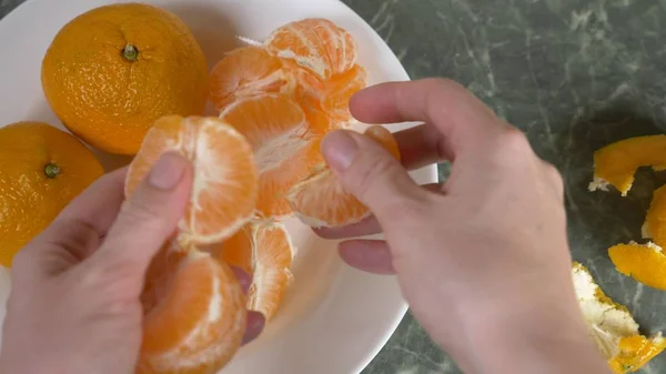 Le mani delle donne sbucciano la buccia dei mandarini, le fette di mandarino sono ammucchiate in una ciotola. . — Foto Stock