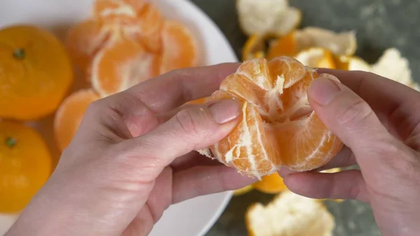 Жіночі руки очищають шкірку мандаринів, скибочки мандарина збирають у мисці . — стокове фото
