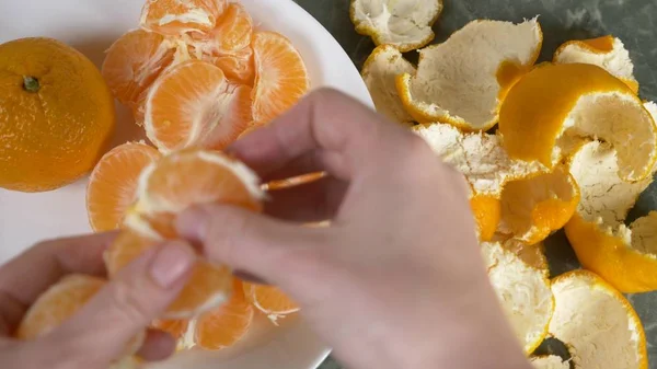 Жіночі руки очищають шкірку мандаринів, скибочки мандарина збирають у мисці . — стокове фото