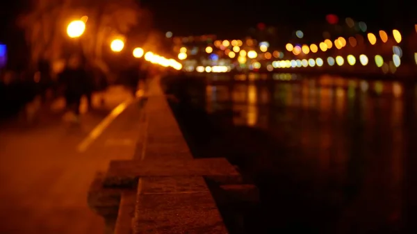 Ludzie spacery wzdłuż nasypu, usiana światła wieczorem. rozmycie. bokeh — Zdjęcie stockowe