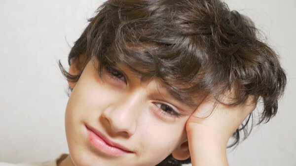 A young boy looks at the camera . the boy laid his head on his palm and looked into the camera.