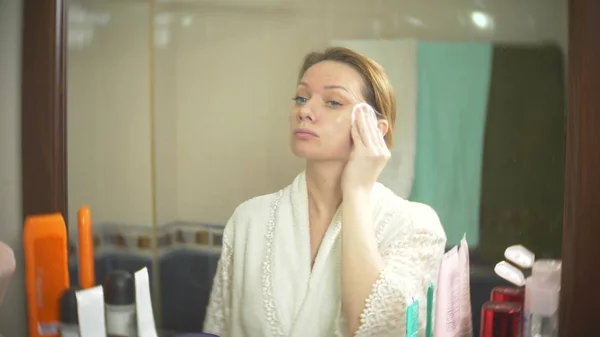 Woman cleaning face with cotton swab in front of the mirror. close-up. background blur. — Stock Photo, Image