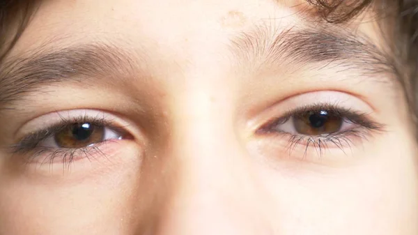 Gli occhi marroni di un ragazzo con lunghe ciglia nere. guarda da sotto un lungo ciuffo riccio. primo piano — Foto Stock