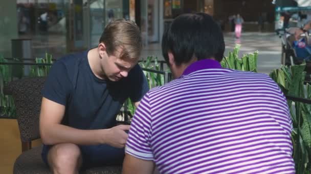 Close-up, bijeenkomst in een café. mannen zaken bespreken zitten in een cafe voor een groot winkelcentrum — Stockvideo