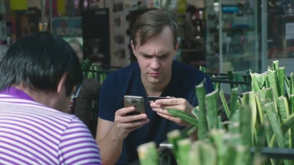 Een man maakt gebruik van zijn bankkaart en telefoon zittend in een café een grote shopping complex — Stockvideo