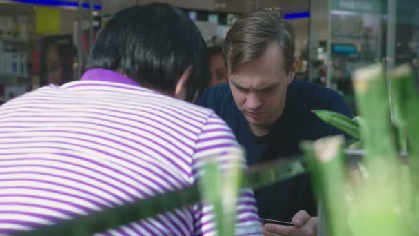 Un hombre utiliza su tarjeta bancaria y teléfono mientras está sentado en un café de un gran complejo comercial — Vídeo de stock