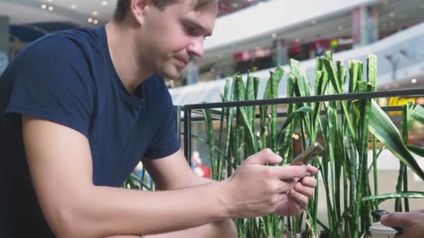 Een man maakt gebruik van zijn bankkaart en telefoon zittend in een café een grote shopping complex — Stockvideo