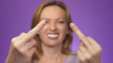 Genç güzel kadın arka planda, bulanık, gülümseyerek. Orta parmak gösterilen elini odak. renkli arka plan.