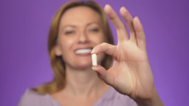 Une jeune femme avec un sourire à dents blanches en arrière-plan est floue, tient une tablette dans sa main. comprimé dans la netteté. concept pharmacologique, vitamines, compléments alimentaires bio-actifs. fond de couleur — Video