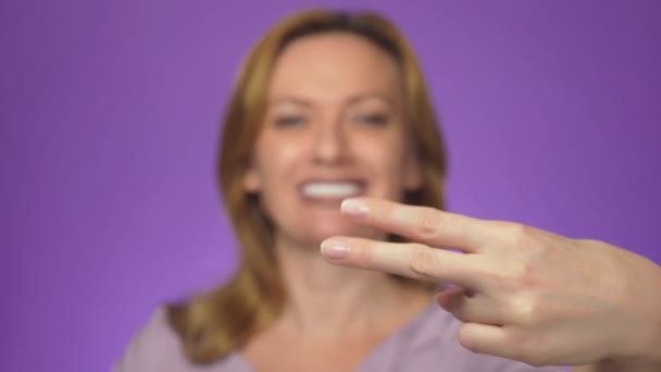 Joven mujer hermosa, borrosa en el fondo, sonriendo. En el centro de atención está su mano mostrando el símbolo de las tijeras. color de fondo — Vídeos de Stock