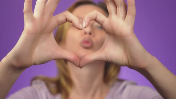 Soins dentaires et blanchiment des dents. La dentisterie et les cosmétiques. Femme souriant en arrière-plan une image floue. dans la netteté des mains d'une fille, ils montrent un signe cardiaque. fond de couleur — Video