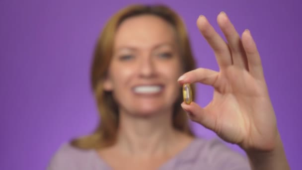 Hälsosam kost mat. Vackra leende ung kvinna håller en fisk olja piller i hennes hand. Närbild. Ta kapsel. Vitamin- och kost-tillskott. färg bakgrunden, oskärpa, 4k — Stockvideo