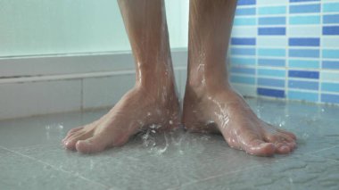 Duşta erkek bacak yakın çekim. Genç adam bir duş alır.