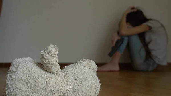 Ein verzweifeltes Kind in Depressionen sitzt an der Wand seines Zimmers und versucht Selbstmord. Daneben steht ein verlassenes Stofftier. — Stockfoto