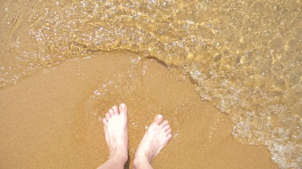 Pés femininos na areia, a onda do mar cobre as pernas femininas — Fotografia de Stock