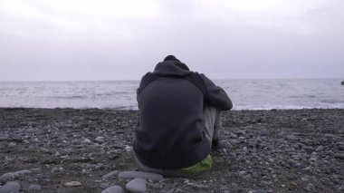 Yalnız bir çocuk sahilde oturuyor.