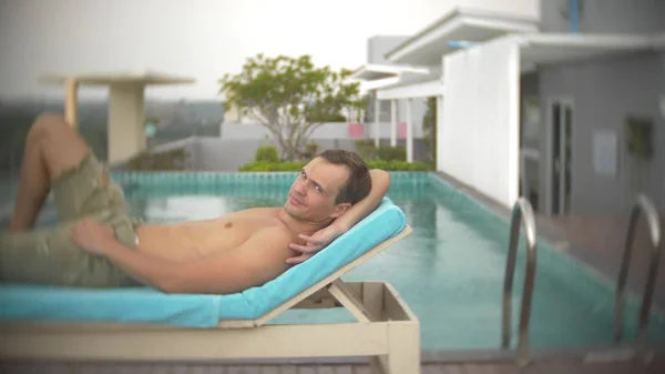Um homem relaxante, banhos de sol nas espreguiçadeiras perto da piscina no telhado com vista para o mar. borrão de fundo — Fotografia de Stock