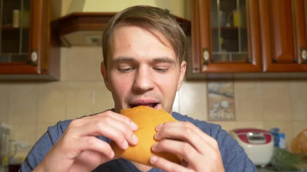 Un hombre come un strudel de manzana con placer, sentado en su cocina . — Foto de Stock