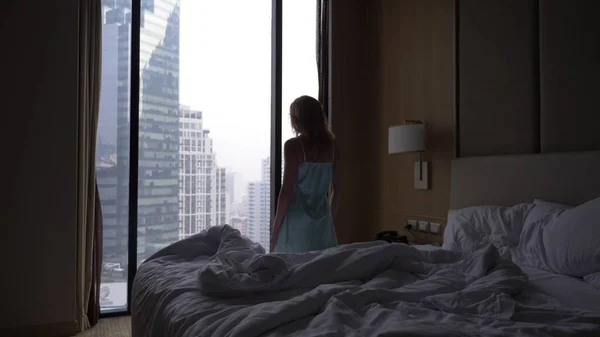 The woman wakes up from sleep and comes to the window with a view of the skyscrapers, slow movement.
