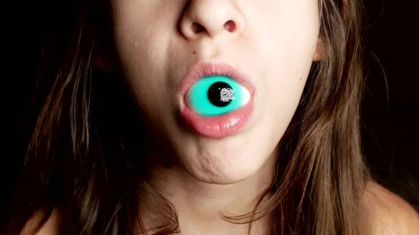 Close-up. a cheerful teenage girl holds large round candies in her mouth, similar to the eyes — Stock Photo, Image