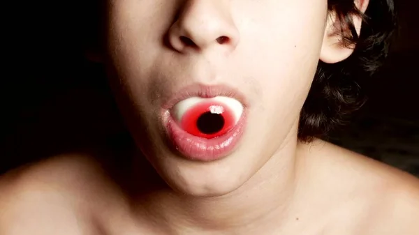 Close-up. Um adolescente alegre segura um grande doce redondo em sua boca, semelhante aos olhos . — Fotografia de Stock