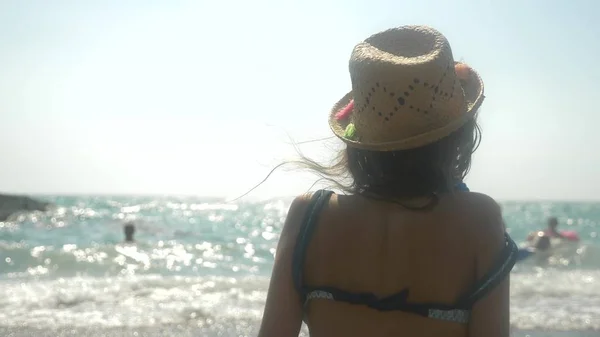 Primer plano. la chica en un sombrero de paja mira las olas del mar. vista posterior — Foto de Stock