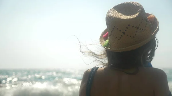 Primo piano. la ragazza con il cappello di paglia guarda le onde del mare. vista posteriore — Foto Stock