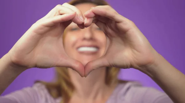 Zahnpflege und Zahnaufhellung. Zahnmedizin und Kosmetik. Frau lächelt im Hintergrund ein verschwommenes Bild. In der Schärfe der Hände eines Mädchens zeigen sie ein Herzzeichen. Farbhintergrund — Stockfoto