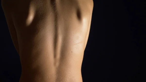Giovane donna con schiena nuda su uno sfondo nero. concetto di salute schiena, colonna vertebrale. copia spazio — Foto Stock