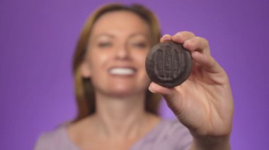 Genç güzel kadın arka planda, bulanık, gülümseyerek. Elini yuvarlak çikolata parçalı kurabiye ile ilgi odağı olduğunu.