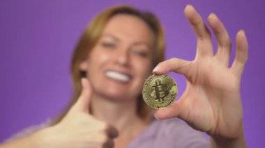 arka plan beyaz dişli bir gülümseme ile genç bir kadın bulanık, onun elinde bir bitcoin altın madeni para almıştır. Bitcoin netlik. renk arka plan