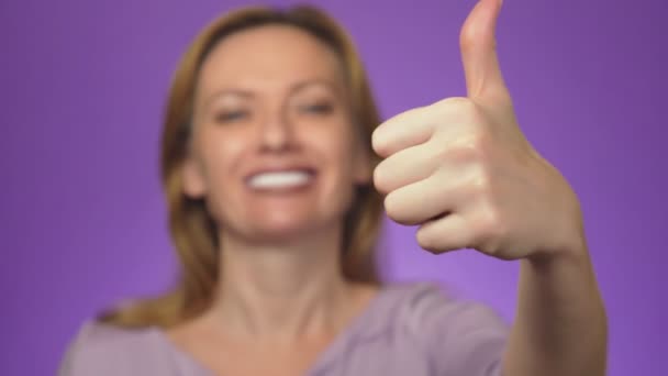 Boldog, fiatal nő, mutatja az ok jele ujjaival és hunyorítva. Háttérszín — Stock videók