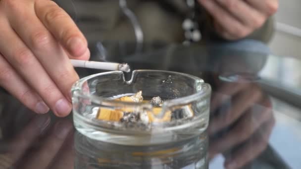 Colillas de cigarrillos de un cenicero de vidrio en una mesa de vidrio al aire libre . — Vídeo de stock