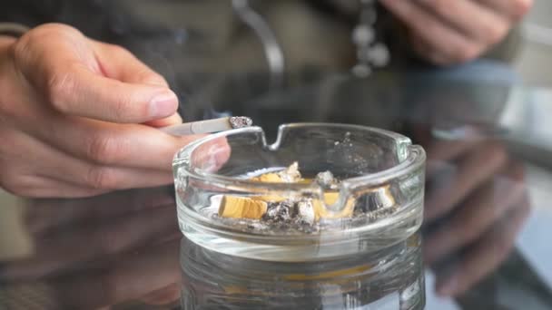 Mégots de cigarette à partir d'un cendrier en verre sur une table en verre à l'extérieur . — Video