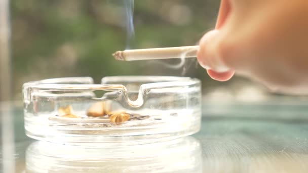 Colillas de cigarrillos de un cenicero de vidrio en una mesa de vidrio al aire libre . — Vídeos de Stock