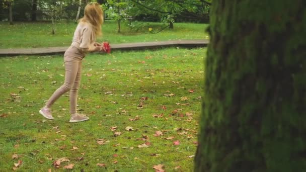 Молода блондинка гуляє по осінньому парку, вона збирає впале кленове барвисте листя — стокове відео