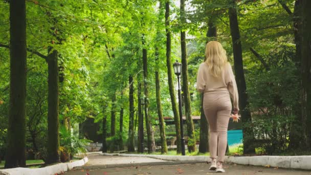 Mladá blond žena chodí přes podzimní park, sbírá barevné listí spadané javor — Stock video