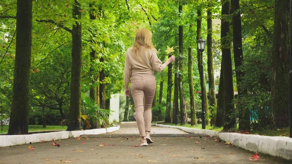 Jonge blonde vrouw doorloopt de herfst park, ze verzamelt gevallen esdoorn kleurrijke bladeren — Stockfoto