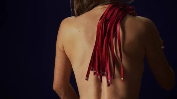 A parte de trás de uma menina magra irreconhecível com uma cintura fina. a mulher chicoteia-se nas costas com um chicote vermelho . — Fotografia de Stock