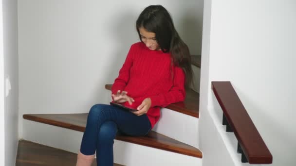 美丽的女孩在红色毛衣和特里袜子和牛仔裤 坐在楼梯上 使用平板电脑 — 图库视频影像