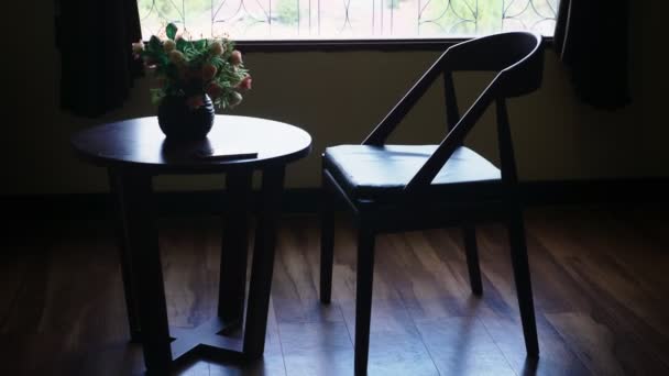Siluetas. silla y mesa con flores en el fondo de una gran ventana. fuera de la vista del follaje verde de los árboles — Vídeos de Stock