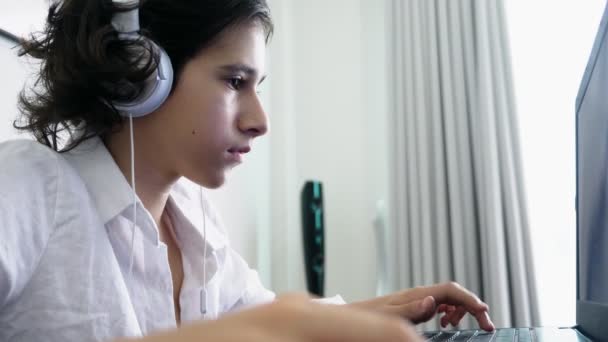 Adolescente juega videojuegos. Ordenador adolescente chico con auriculares mirando a la pantalla del ordenador portátil — Vídeo de stock