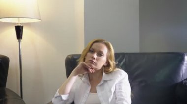 Onun oturma odasında büyük siyah deri sandalyede oturan beyaz ev elbiseli zarif bir kadın hakkında bir şey düşünüyorum, kameraya bakıyor ve gülümsüyor. kopya alanı