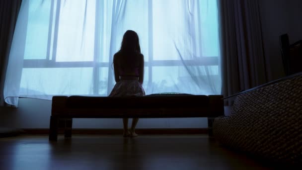 Pequeno adolescente olhando para fora da janela em mau tempo, silhueta de uma adolescente frágil no fundo de uma grande janela — Vídeo de Stock