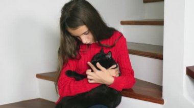 Gülümseyen ve bir kedi yavrusu kucağında tutan güzel genç kız kırmızı kazak ve terry çorap ve kot, merdivenlerde, oturma.